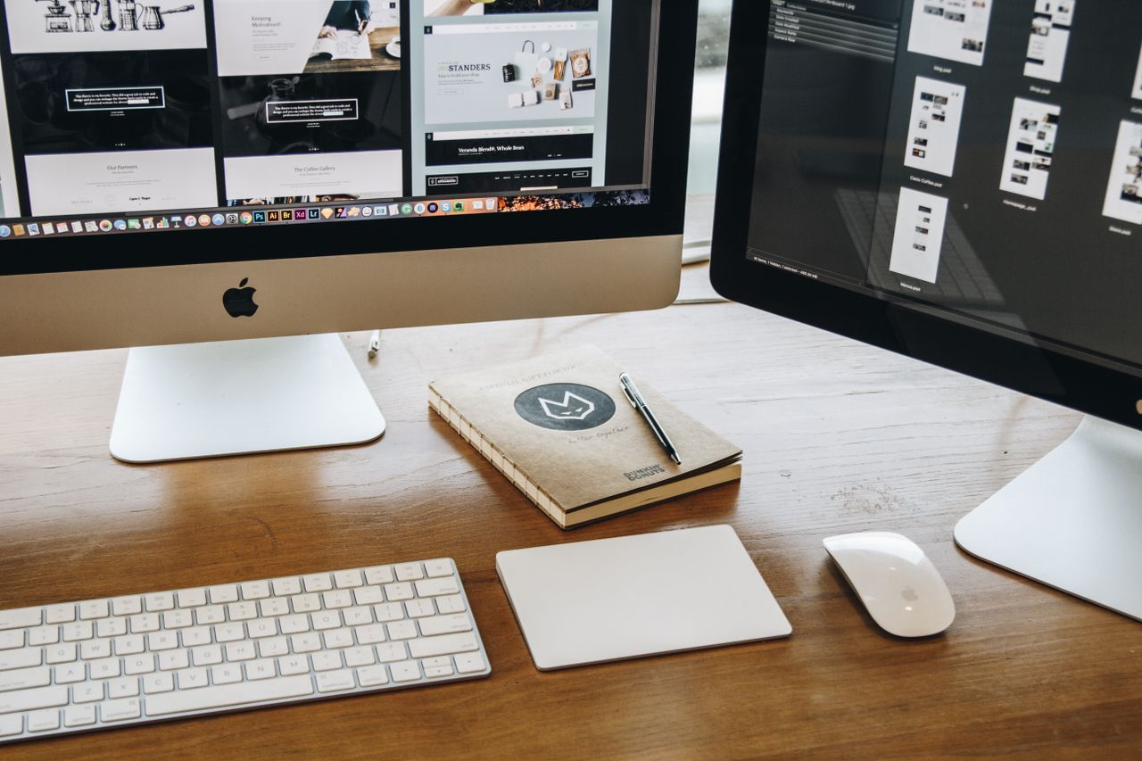 Un bureau épuré équipé de deux écrans, d’un clavier, d’une souris et d’un carnet, pensé pour la productivité.